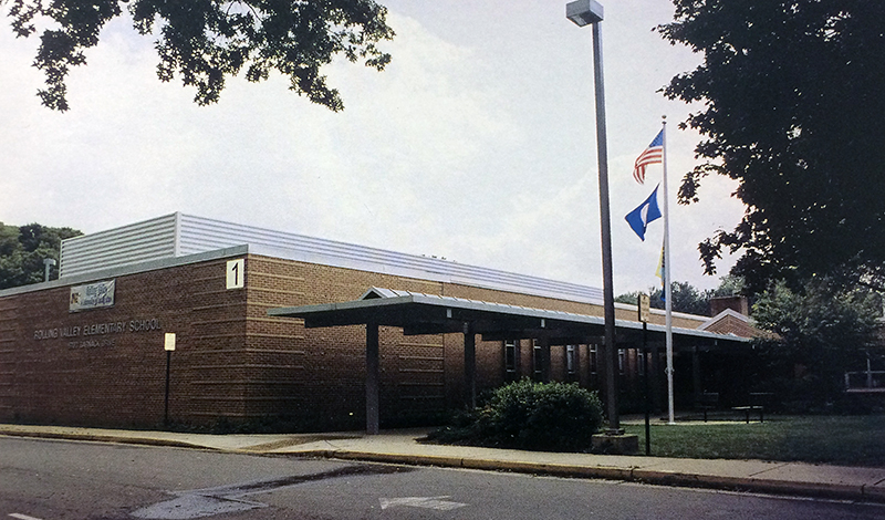Color yearbook photograph of the front entrance of Rolling Valley Elementary School. The classroom wing to the left of the main entrance has been expanded and an awning now covers the sidewalk leading to the front doors. 