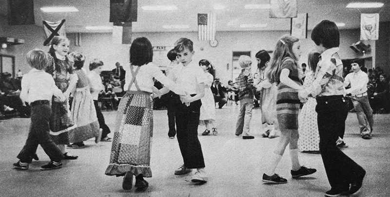 Black and white photograph from our 1977 to 1978 yearbook of children square dancing in the multi-purpose room. 